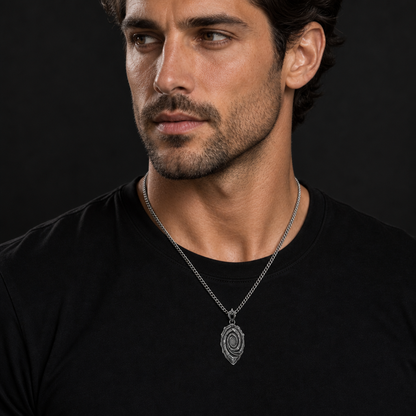 Oxidized 925 sterling silver pendant necklace with a layered spiral relief, central oval motif, angular raised highlights, pointed lower edge, and curb chain on a black background.