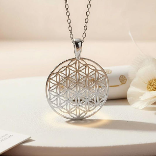 Silver Flower of Life Necklace with a round openwork interlocking-circle pendant beside a white flower